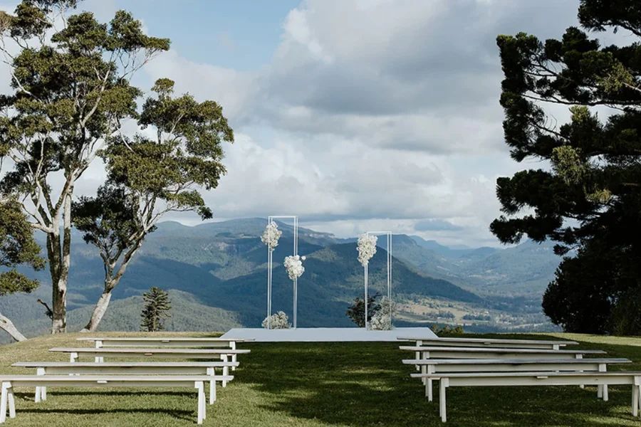 A wedding ceremony is taking place in a field with mountains in the background.
