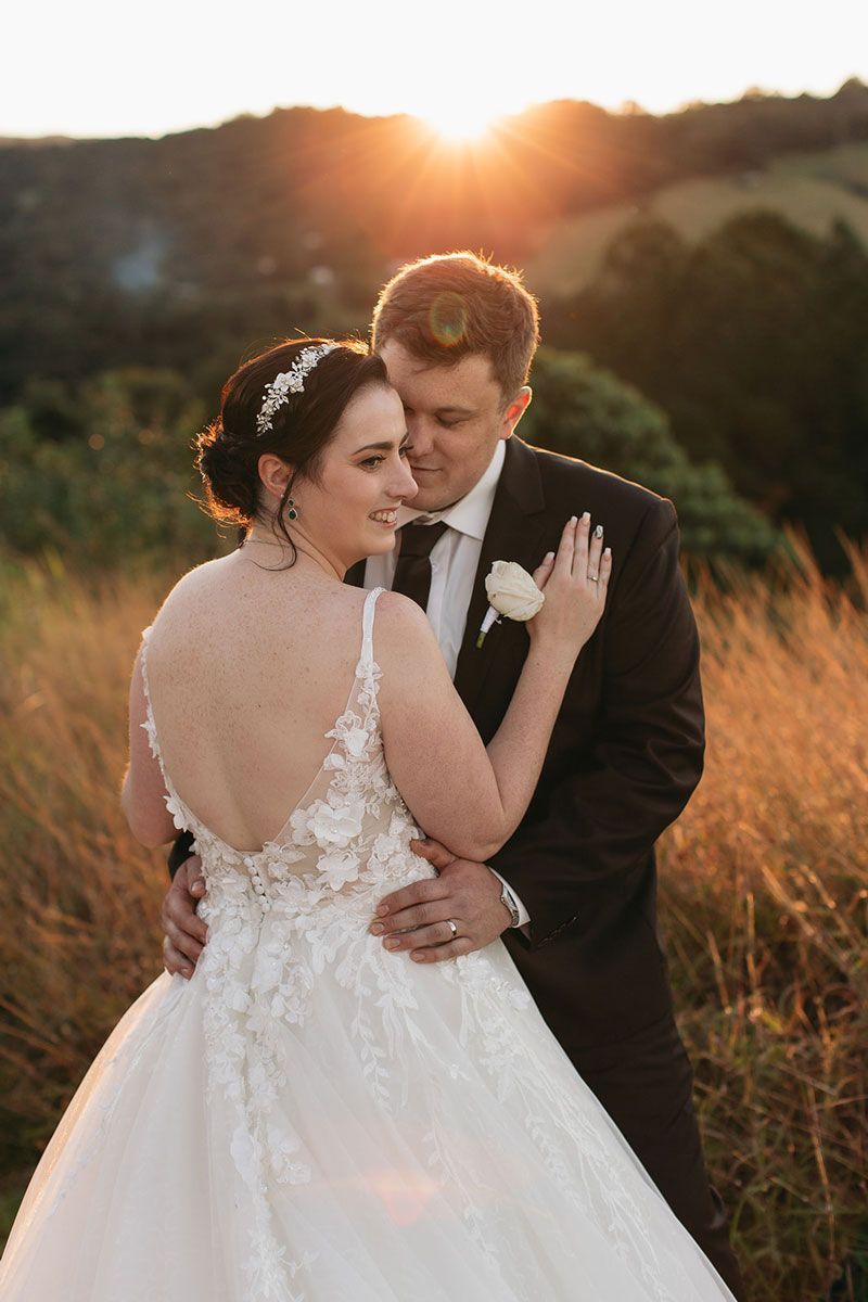 A bride and groom are posing for a picture in a field at sunset.