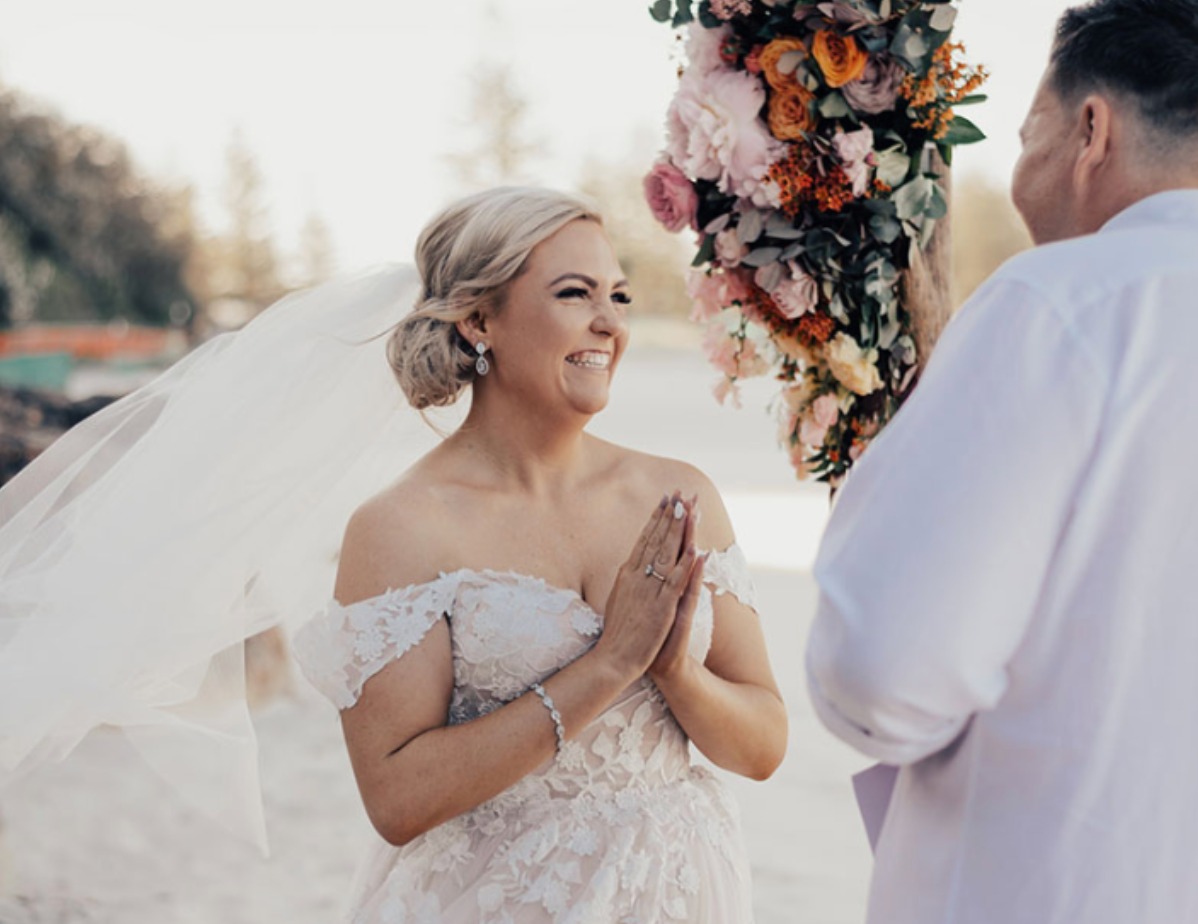 A bride and groom are holding hands during their wedding ceremony on the beach.