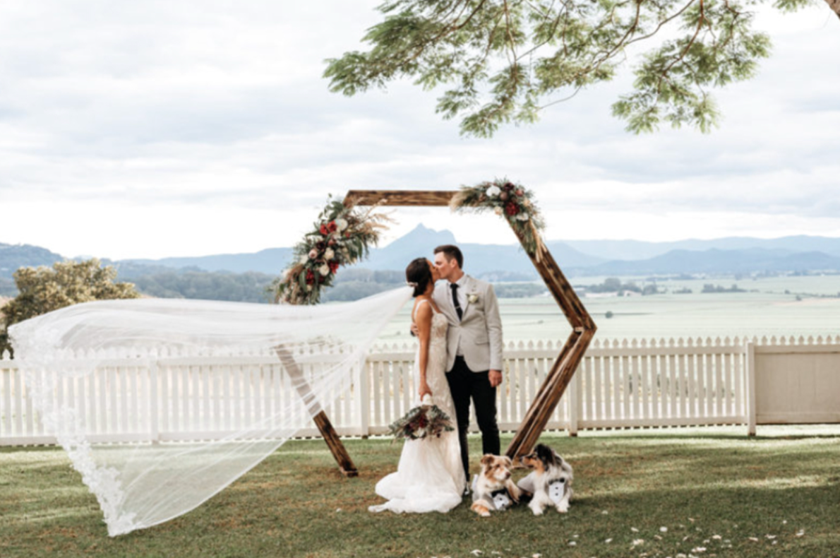 A bride and groom are kissing under a wooden arch.