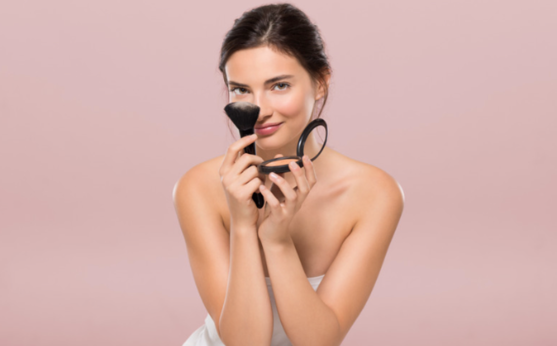 A woman is applying makeup to her face with a brush and a mirror.