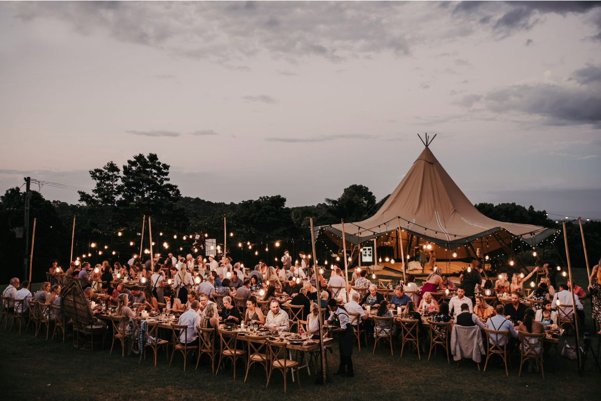 A large group of people are sitting at long tables under a tent.