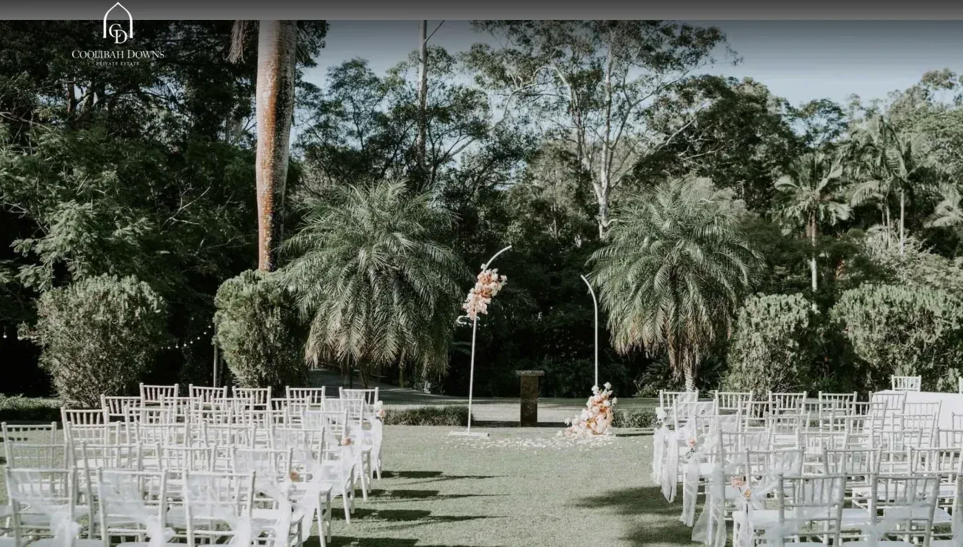 A row of white chairs are lined up in a lush green field.