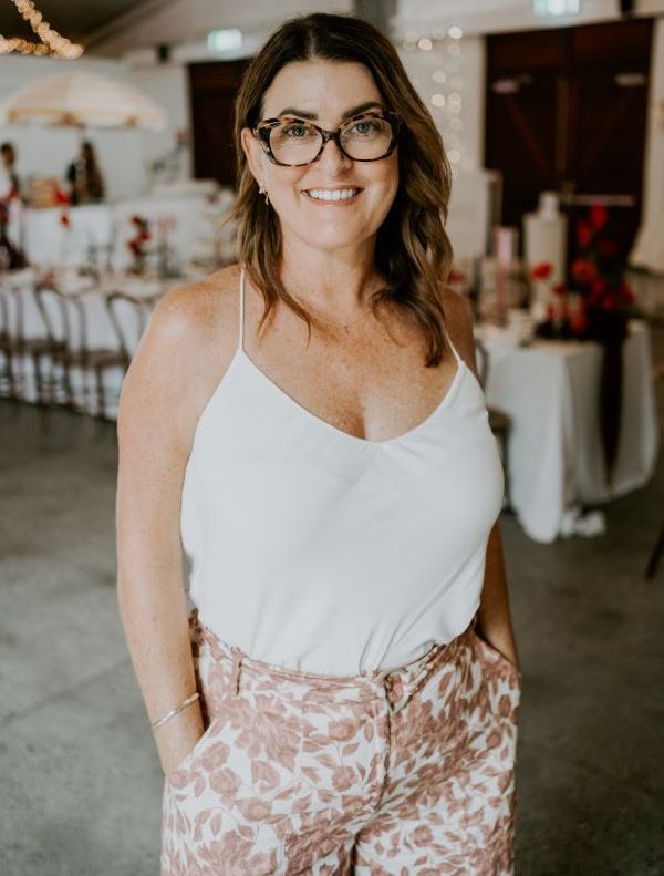 A woman wearing glasses and a white tank top is standing in a room with her hands in her pockets.