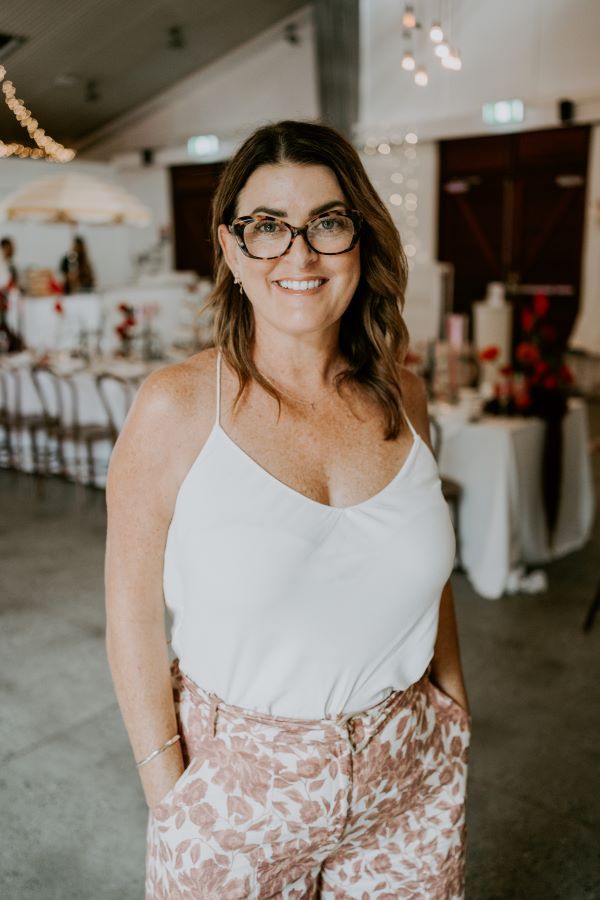 A woman wearing glasses and a white tank top is standing in a room with her hands in her pockets.