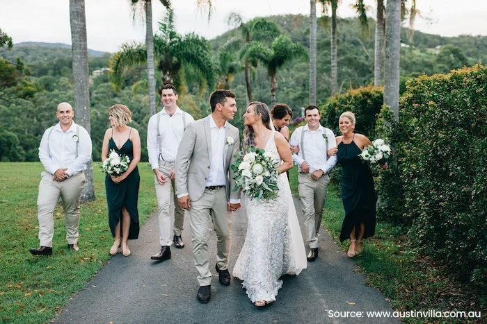A bride and groom are walking down a path with their wedding party.