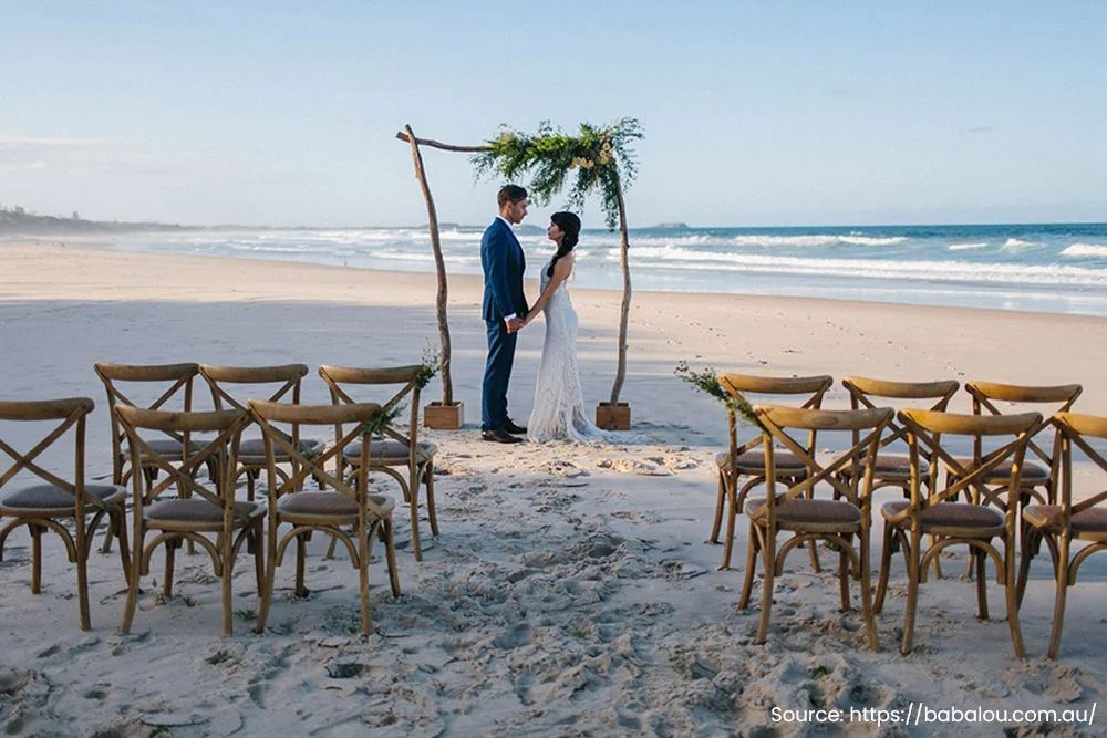 A bride and groom are standing on a beach holding hands.