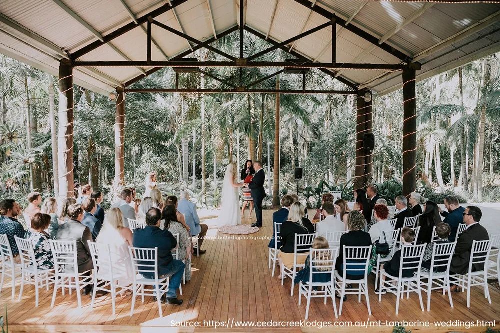 A bride and groom are getting married under a canopy in front of their wedding guests.