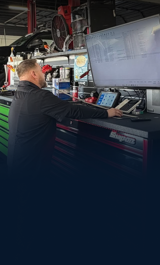 Technician working at a console beside a large monitor in a dim control room | Dunedin Total Car Care