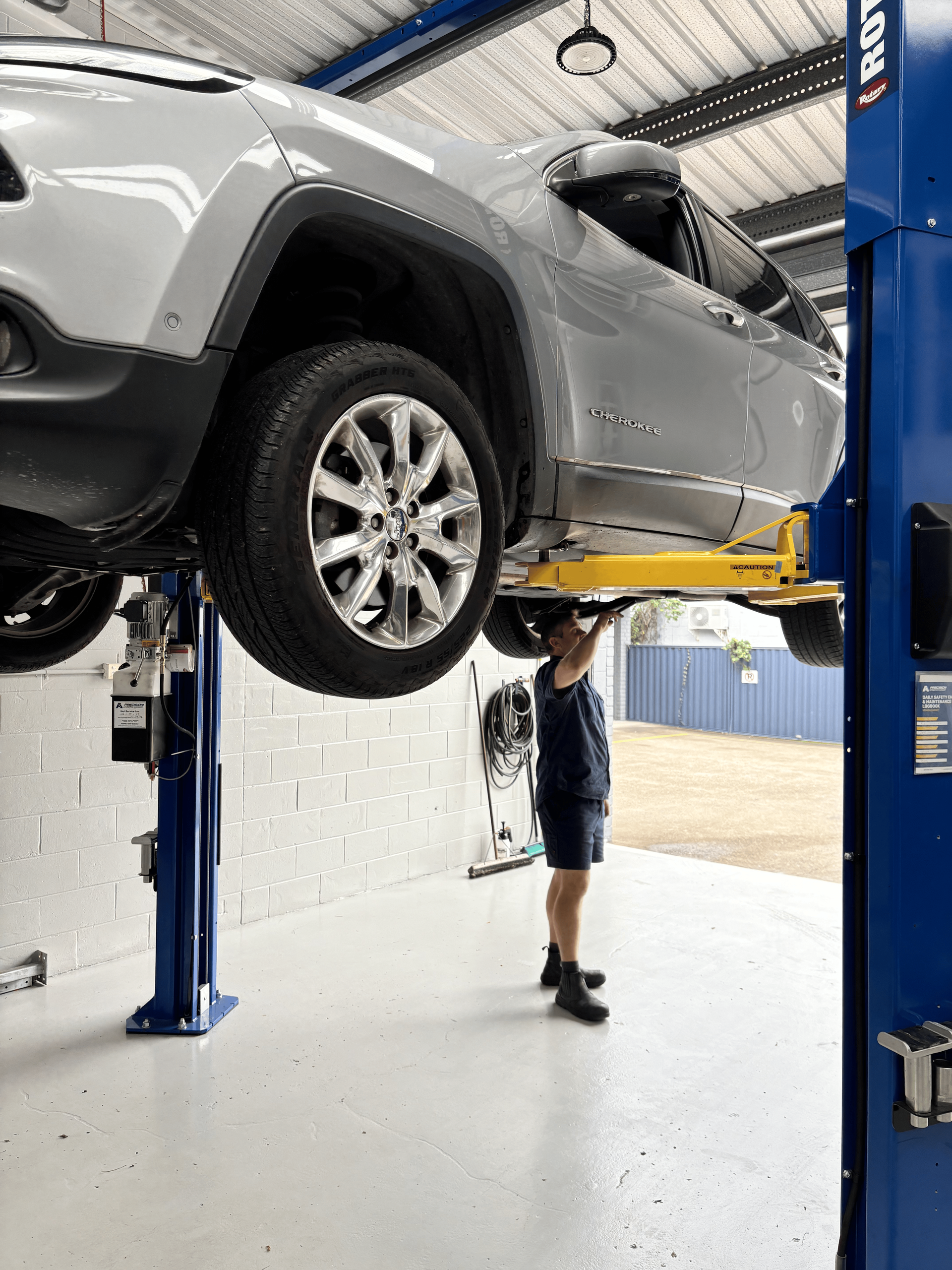 A man is working on a car on a lift in a garage. — Sure Stop Automotive Centre In Nerang, QLD