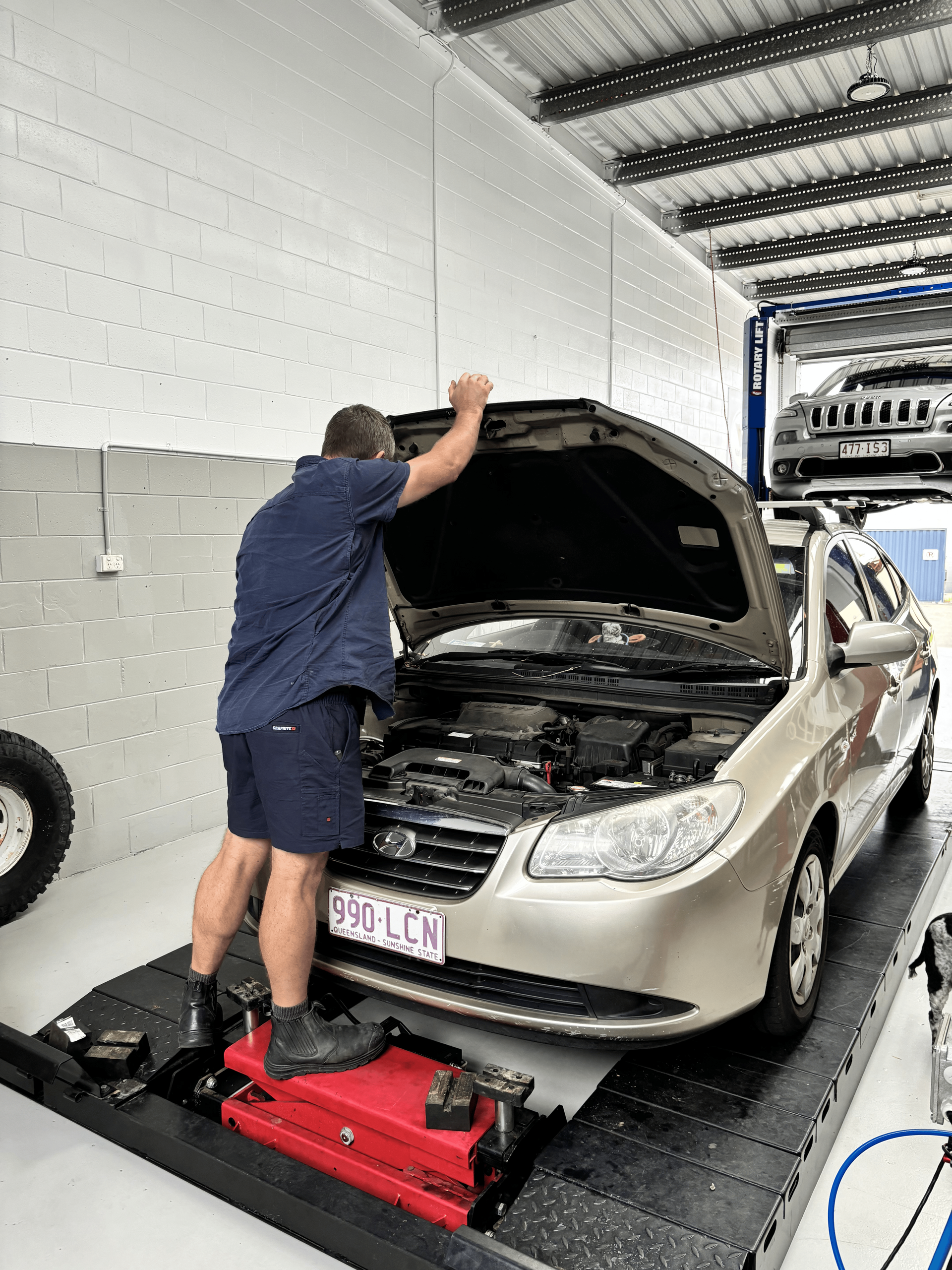 A man is working on a car in a garage with the hood open. — Sure Stop Automotive Centre In Nerang, QLD