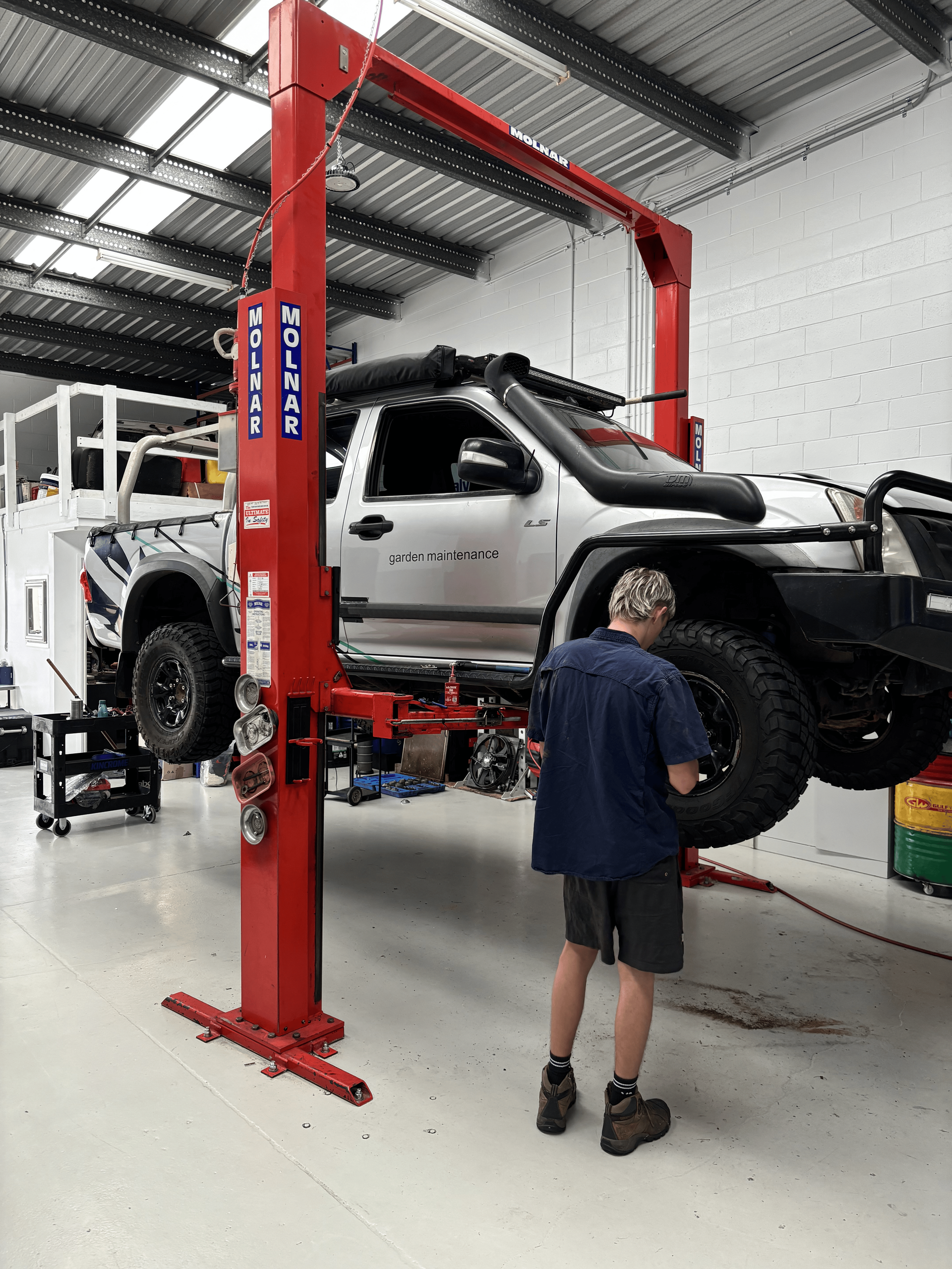 A man is working on a truck on a lift in a garage. — Sure Stop Automotive Centre In Nerang, QLD