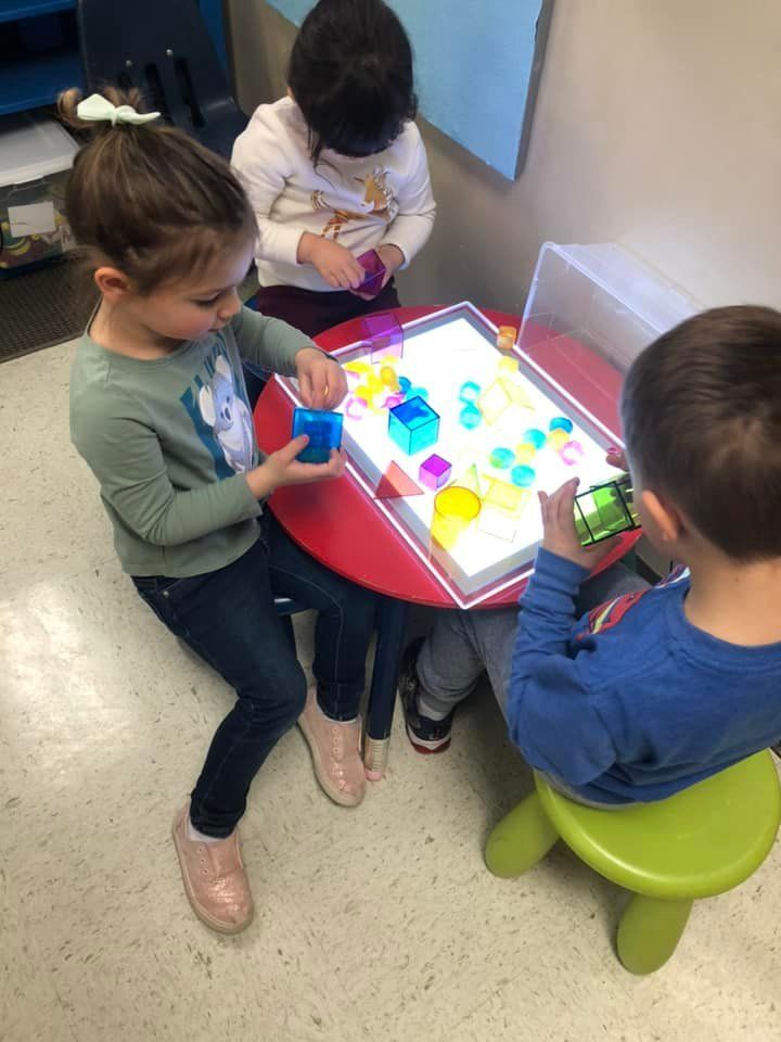 A group of children are playing with blocks on a light table.