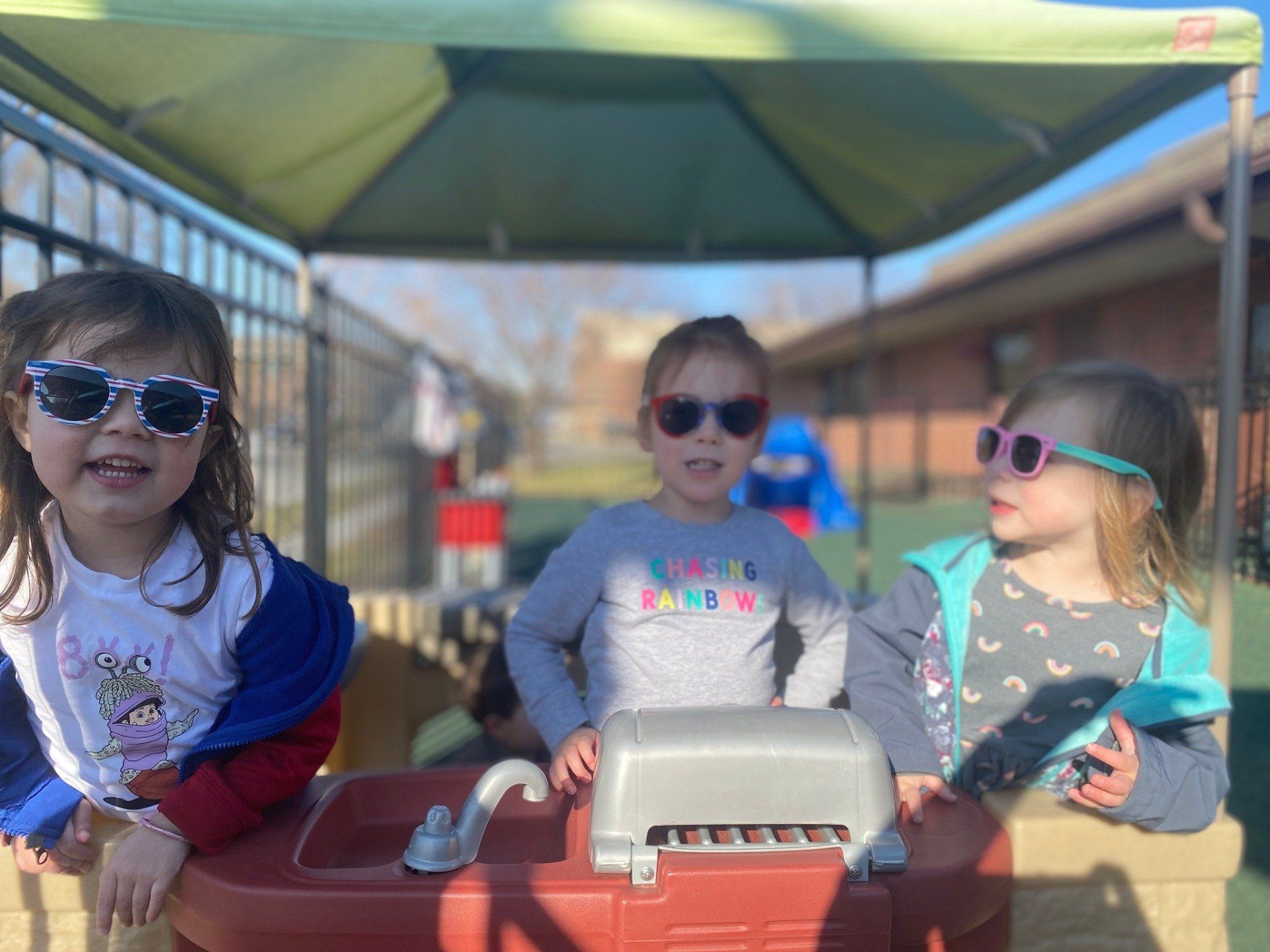 Three little girls wearing sunglasses are sitting under a canopy.