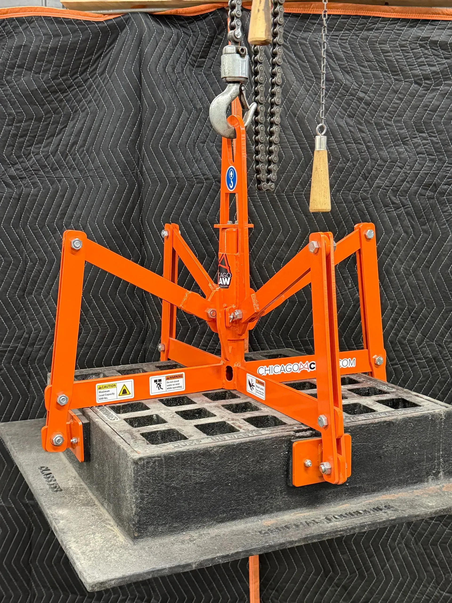 Orange lifting rig holding a cinder block on a platform, with chains hanging above