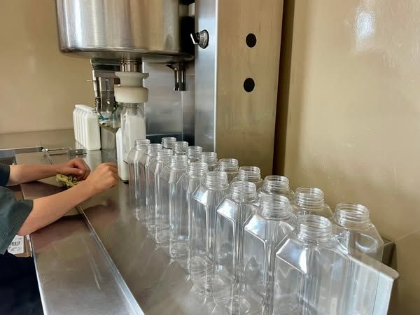 Person filling clear plastic bottles with liquid on an industrial bottling line