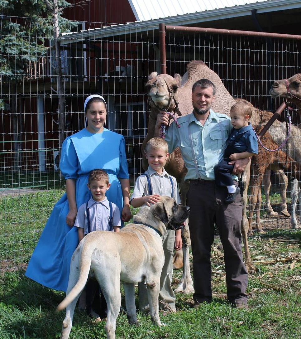 Family standing with three children and two goats outside a barn on a farm