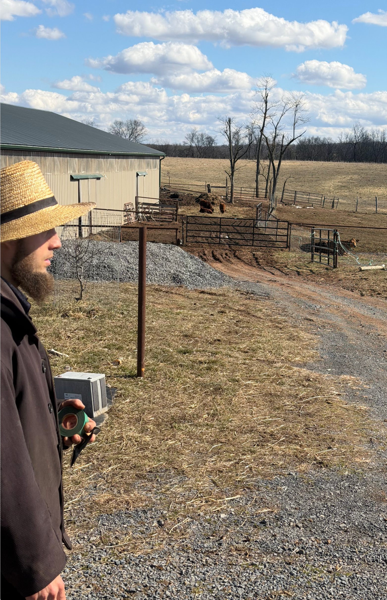 Person in a knit hat walking beside a gravel path near a shed under a cloudy sky.