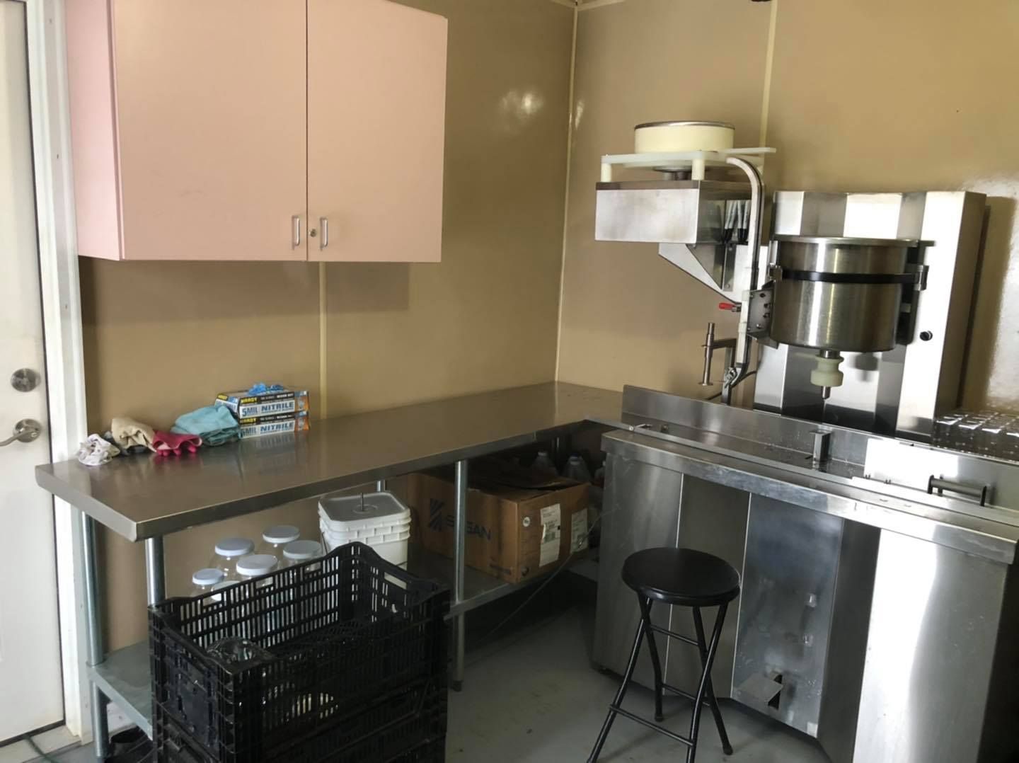 Small kitchen with stainless steel counters, cabinets, and a black stool beside a door.