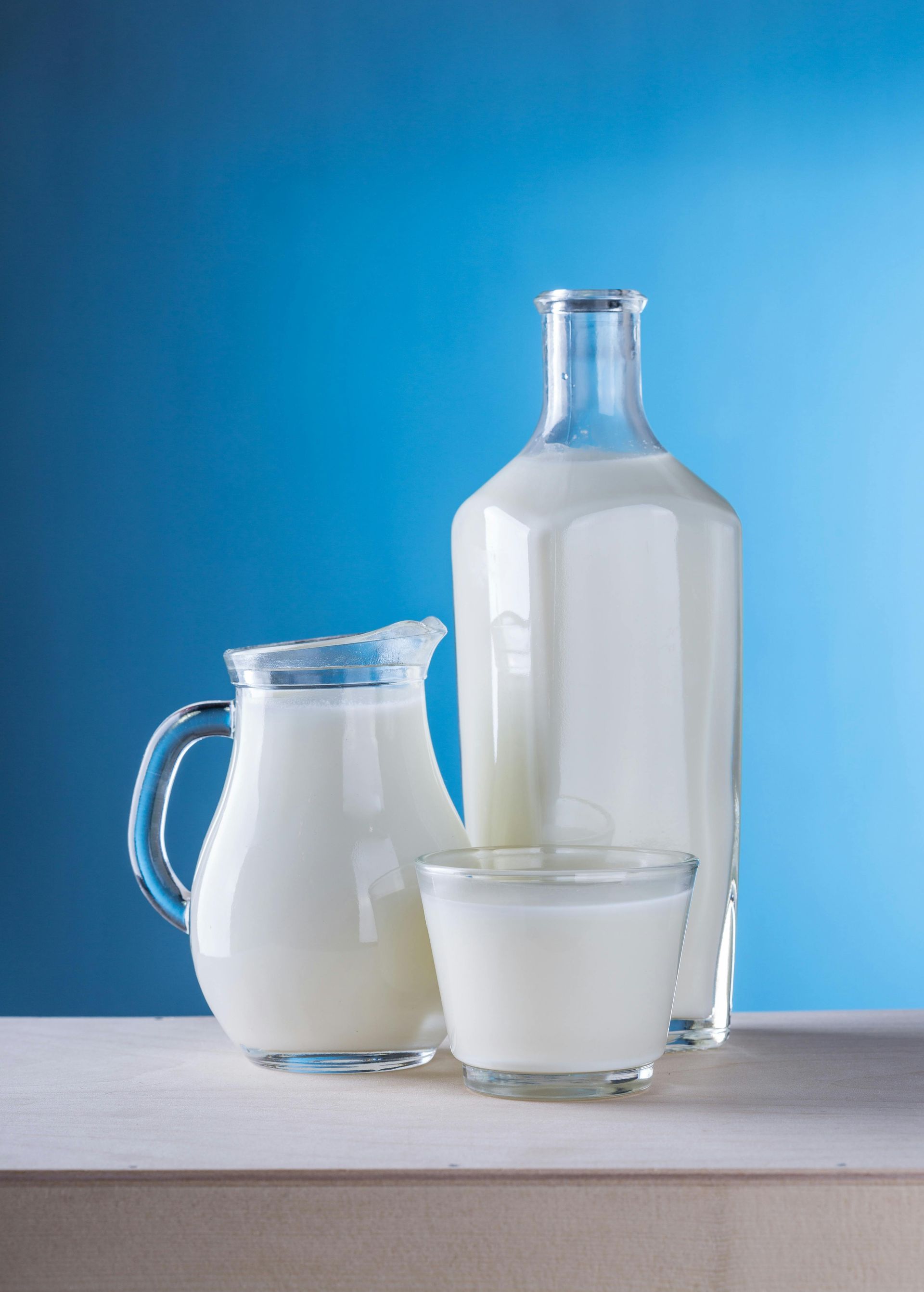 Milk bottles and a glass of milk on a table against a blue background