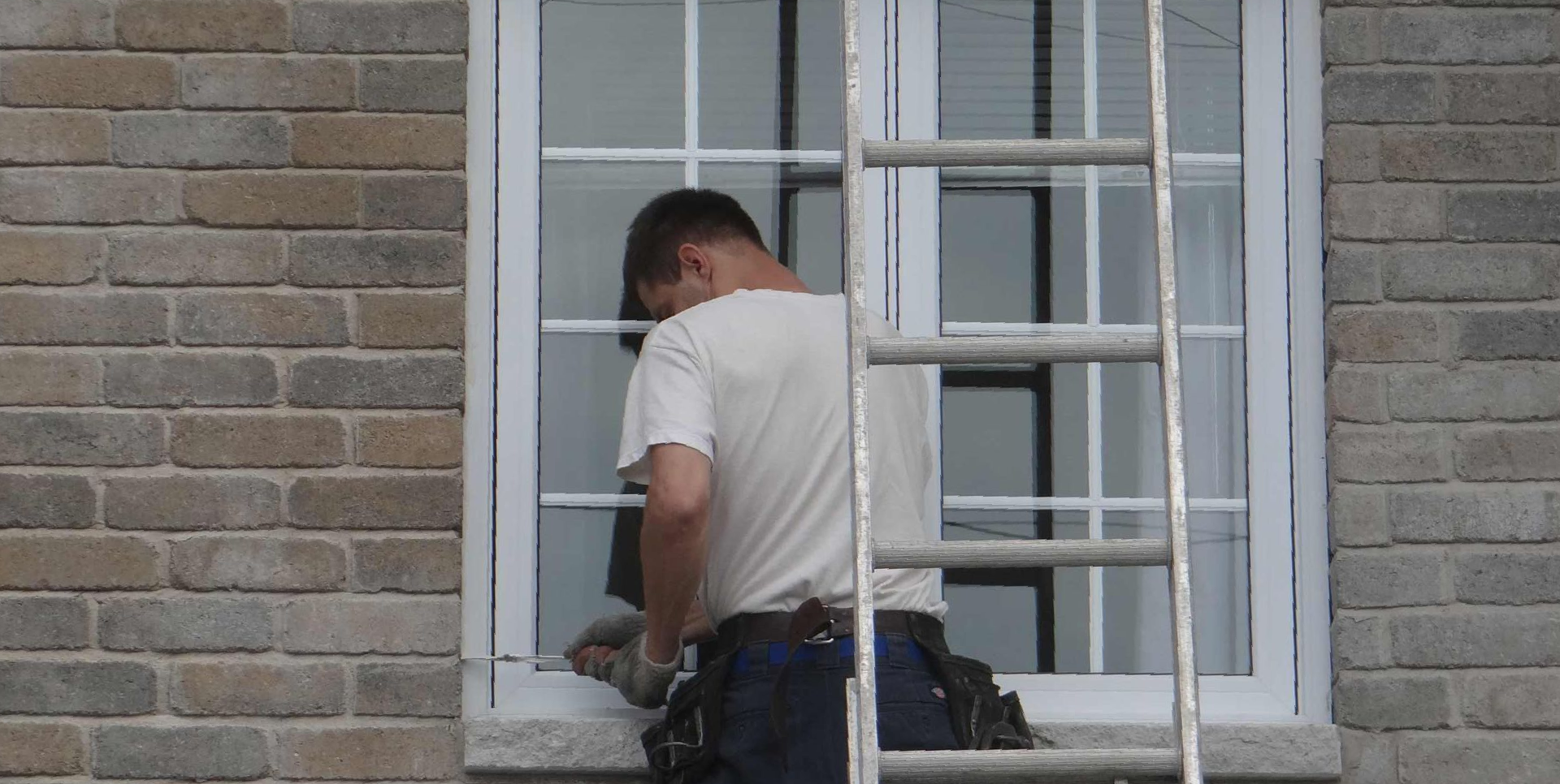 Une personne sur une échelle nettoie une fenêtre d'un bâtiment en briques.