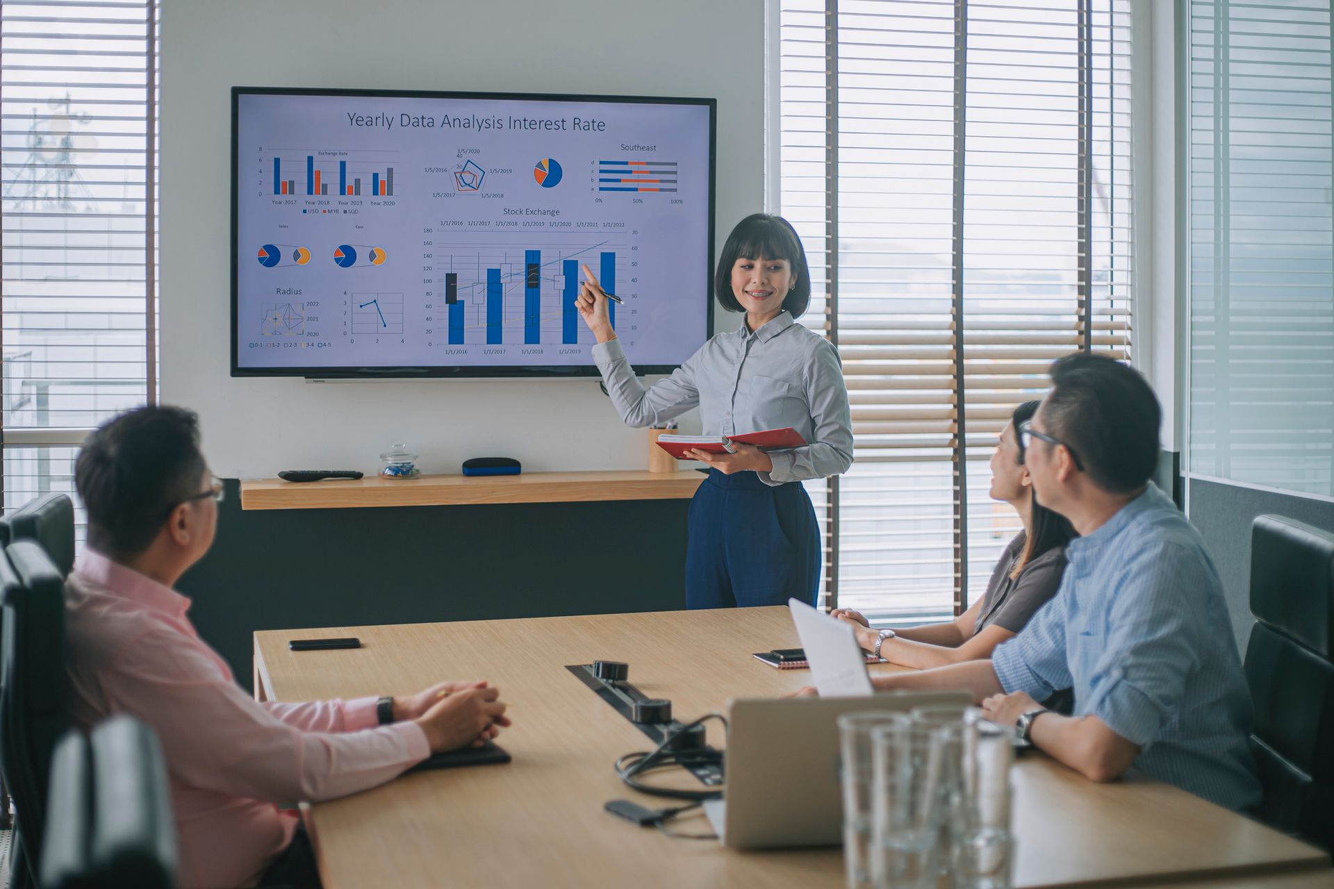 Woman presenting financial data on a screen to colleagues in a conference room.