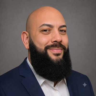 Man in blue suit, orange tie, bald head, goatee, smiling.