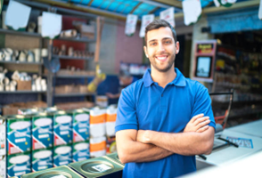 Man in blue shirt, arms crossed, smiling in hardware store, paint cans in foreground.