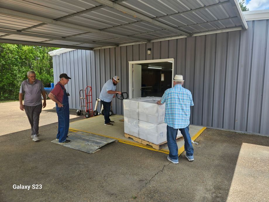 Four people load white crates near a warehouse loading dock under a metal awning.