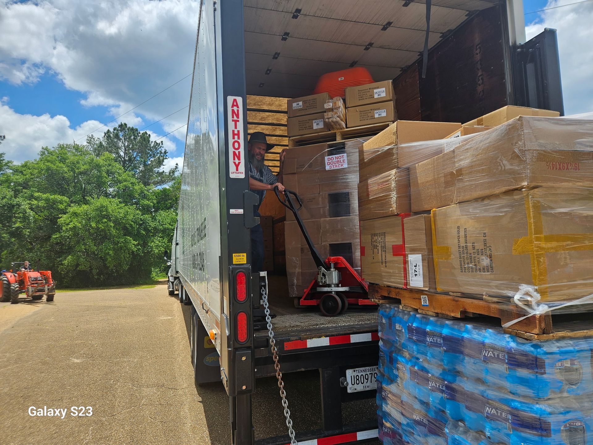 Cargo truck loaded with stacked boxes and pallets, forklift inside at a warehouse loading area