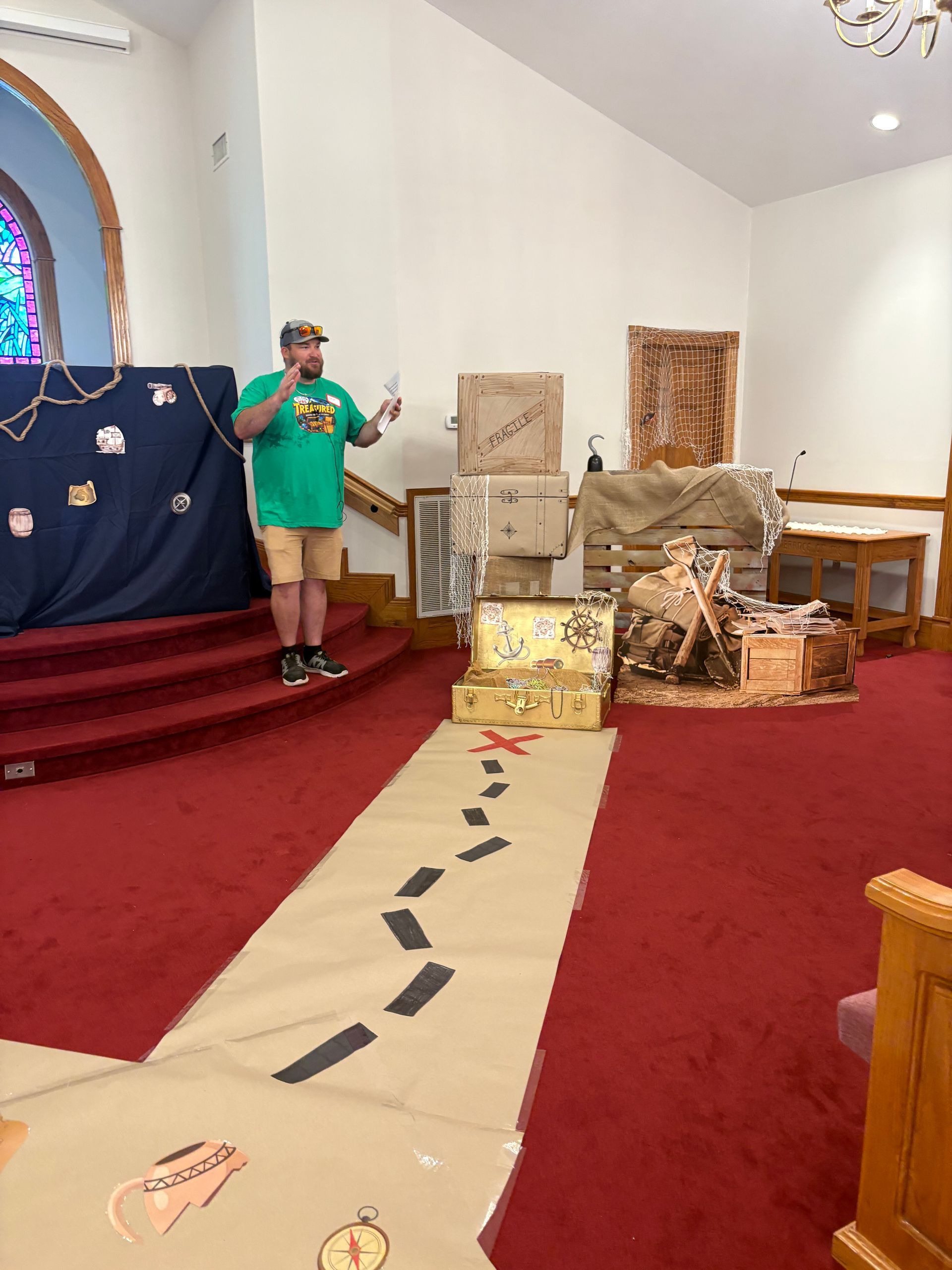 Red-carpeted church interior with a person in green beside a display of decorative items and a stone path aisle