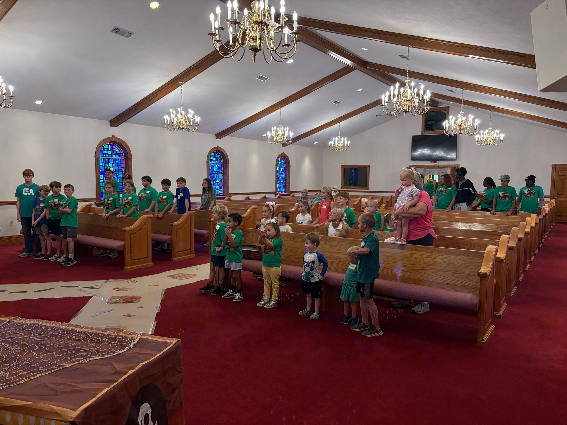 People standing in a church sanctuary with wooden pews, stained glass windows, and a red carpet.