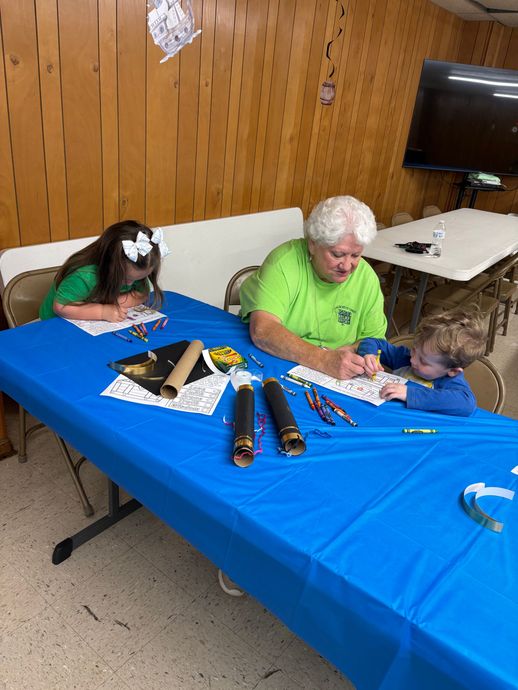 Two people decorating a blue table at a community event, with craft supplies and candles nearby.
