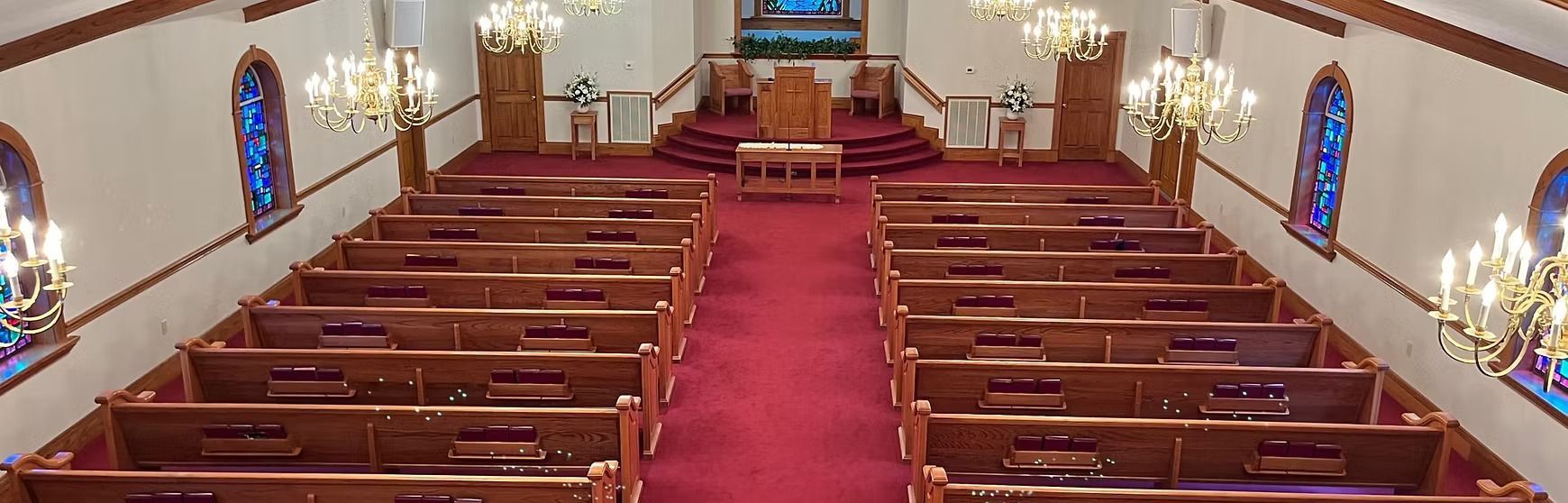 Empty church interior with wooden pews, red carpet aisle, and stained-glass windows