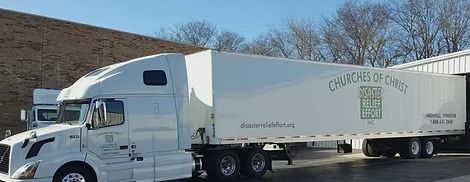 White semi-truck hauling a long trailer labeled “Campers for Christ” on a sunny roadside.