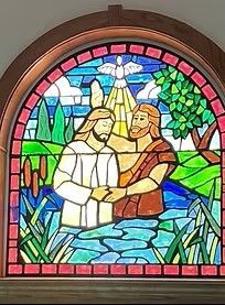 Two robed figures clasp hands in a colorful stained-glass window with a dove and mountains behind them