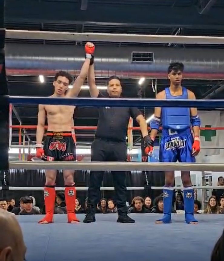Referee raises winner’s arm in a boxing ring, with the other fighter standing beside him.