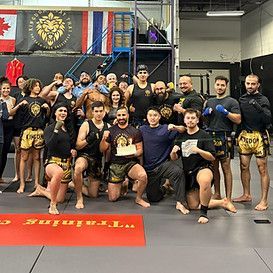 Kingdom Muay Thai in Richmond Ontario Group of martial artists posing in a gym, many in black and gold shorts, holding a trophy.