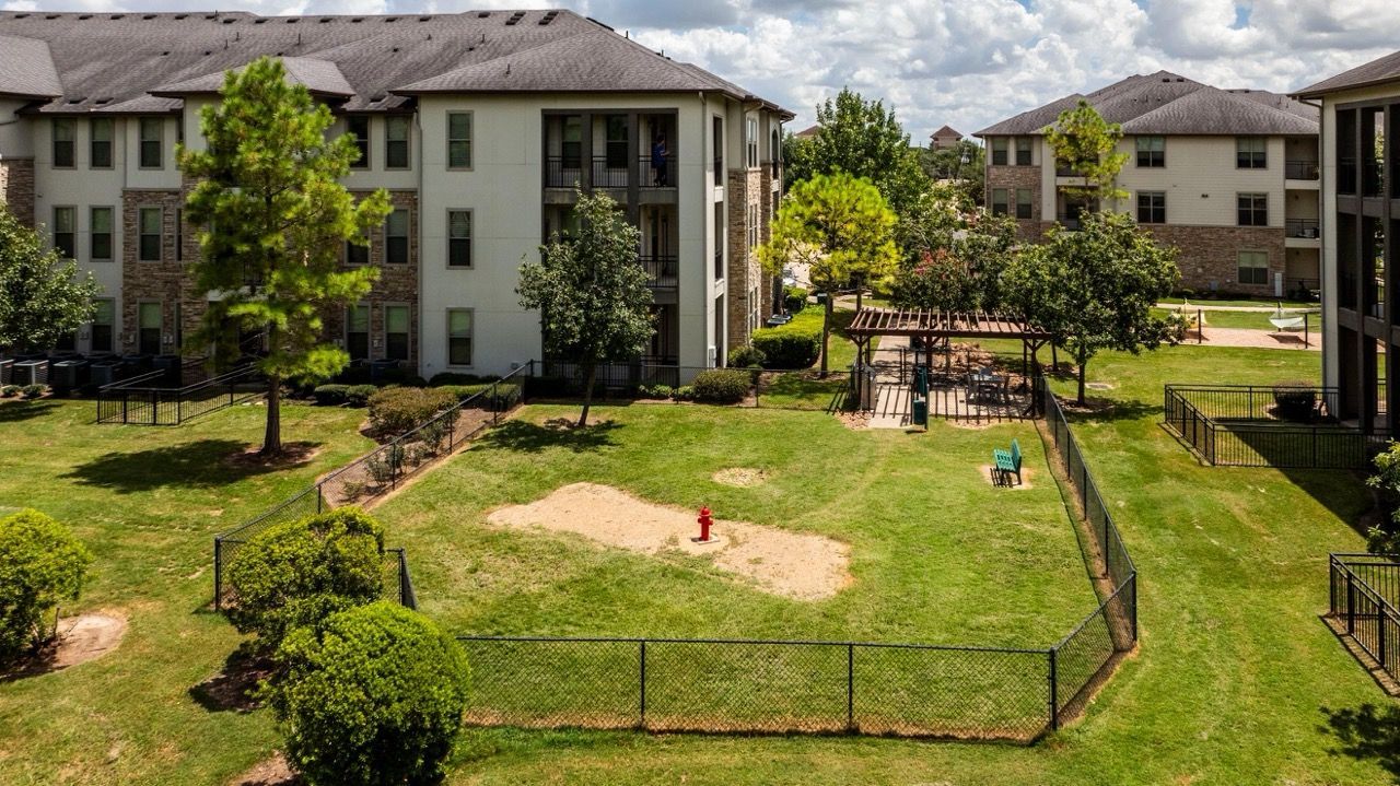 Aerial view of a multi-building apartment complex courtyard with trees, gazebo, and grassy play area.