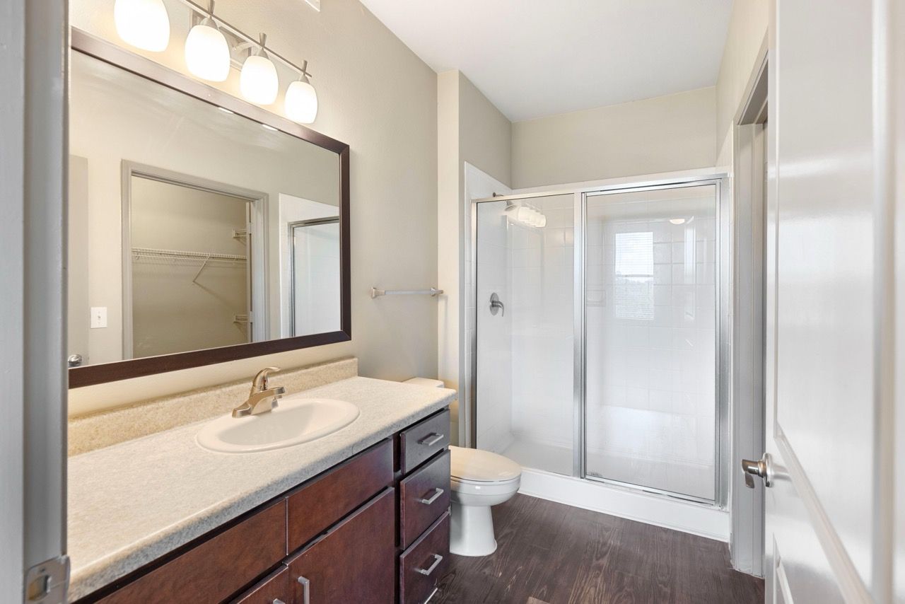 Bathroom in an apartment with a single vanity, mirror, toilet, and glass shower.