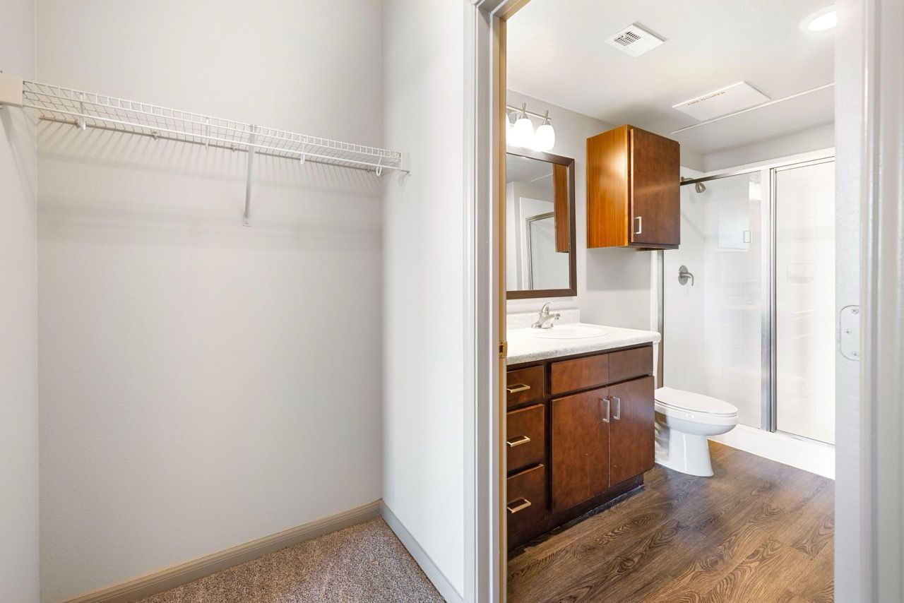 Bathroom in an apartment with a wooden vanity, sink, mirror, shower, toilet, and closet.