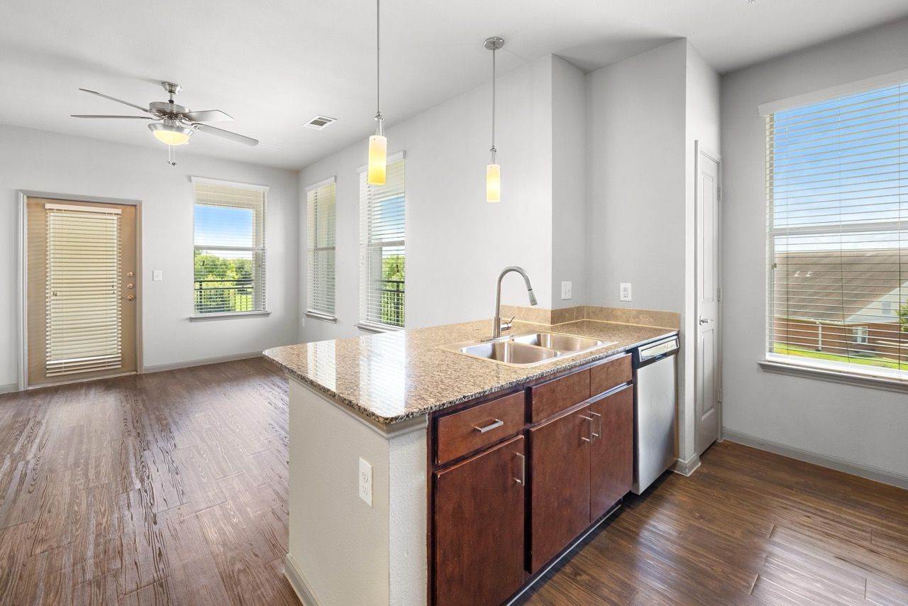 Open-concept kitchen with granite island, double sink, wood cabinets, dishwasher, and large windows.