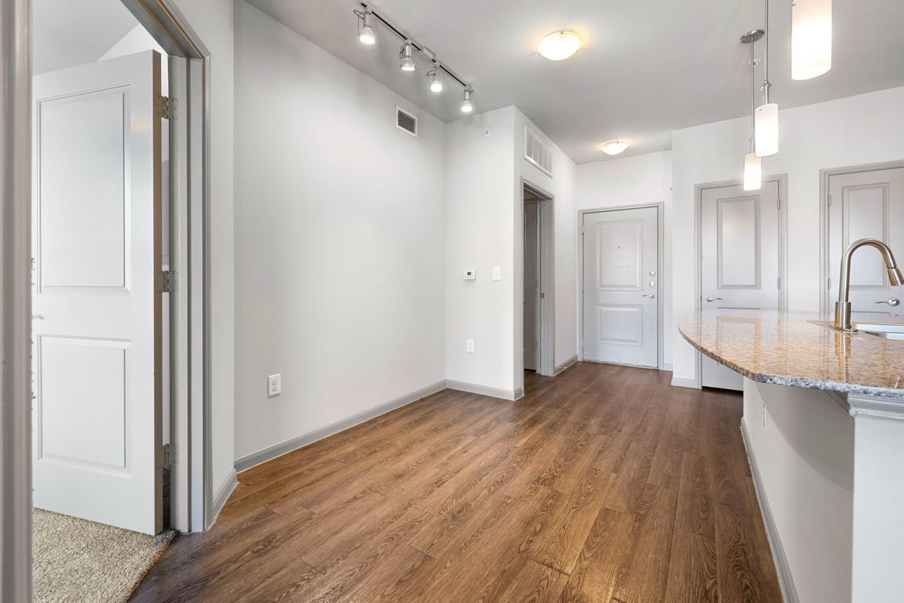 Bright interior of an apartment with hardwood flooring, white walls, and a granite kitchen island.