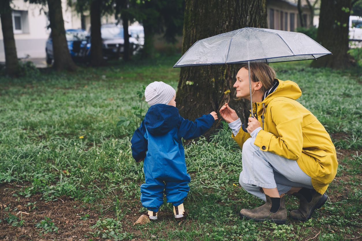 A woman is kneeling down next to a little boy under an umbrella.