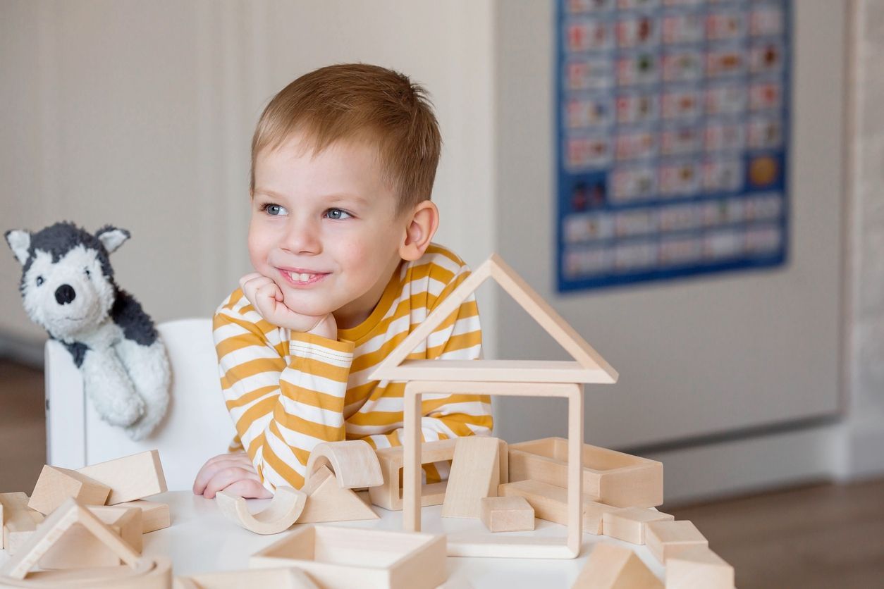 A young boy is sitting at a table with wooden blocks and a stuffed animal.