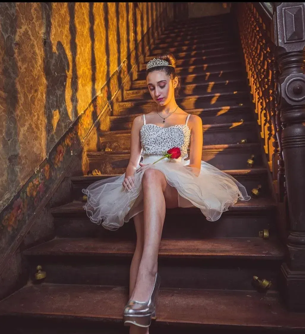 Mujer con vestido blanco sentada en unas escaleras, mirando hacia abajo, con una cálida iluminación ámbar