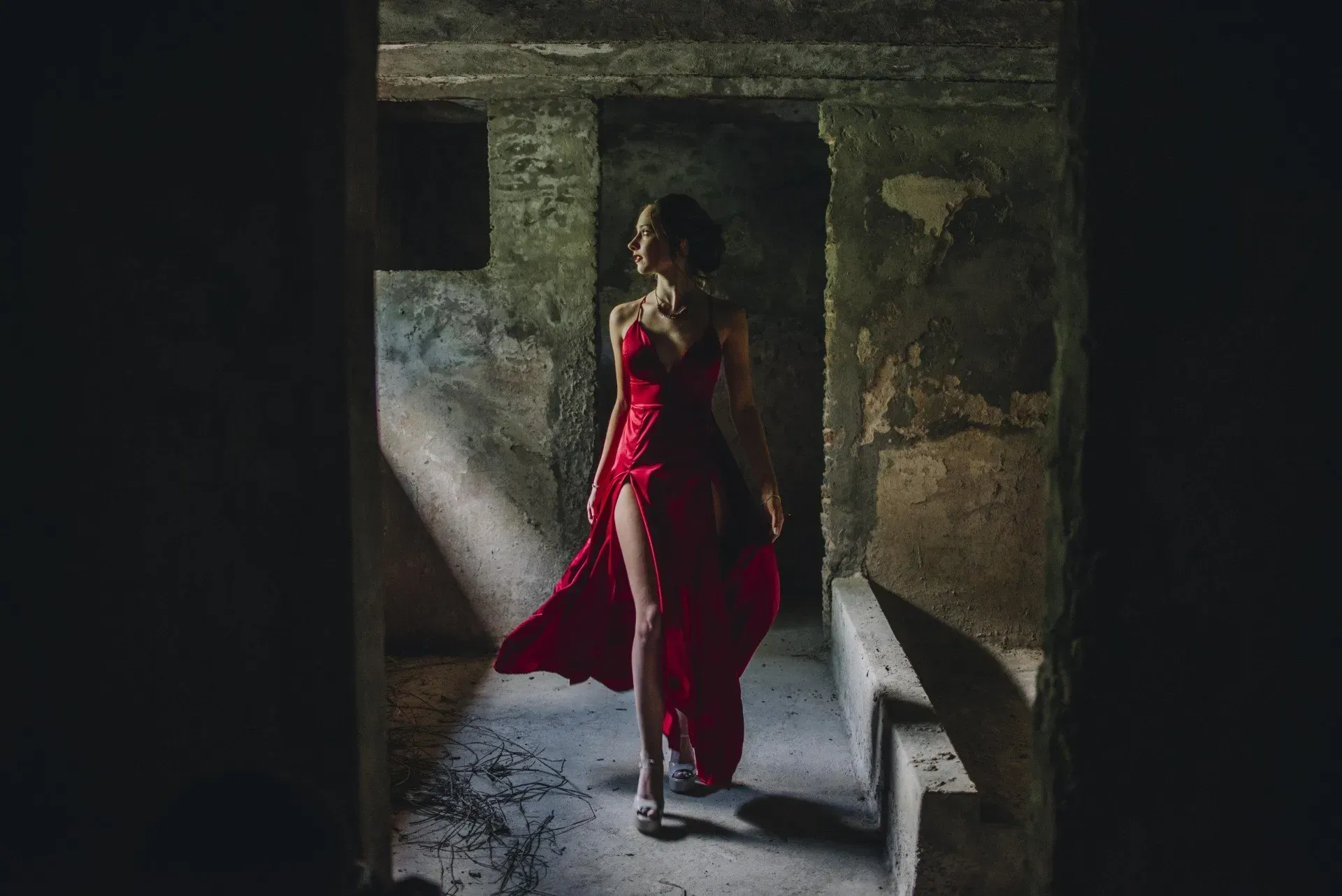 Mujer con un vestido rojo de pie en un portal de piedra poco iluminado, a contraluz por la luz del día.