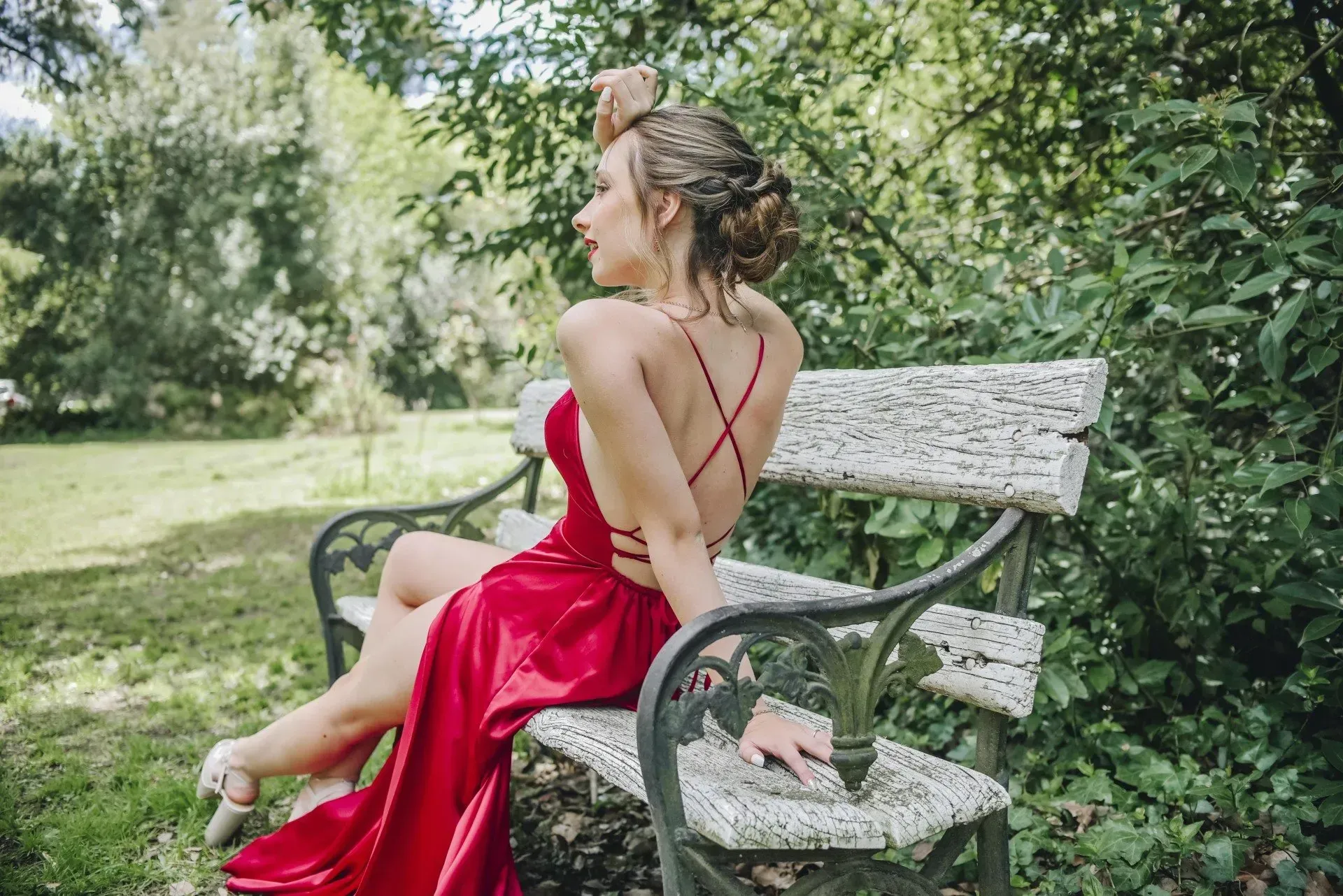 Mujer con vestido rojo recostada en un banco de un parque en un jardín frondoso.