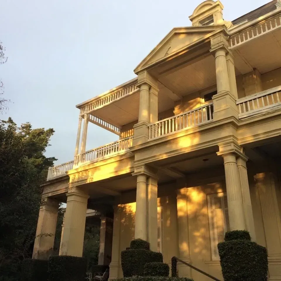 Gran casa histórica con columnas blancas y balcones iluminados por la cálida luz del atardecer.