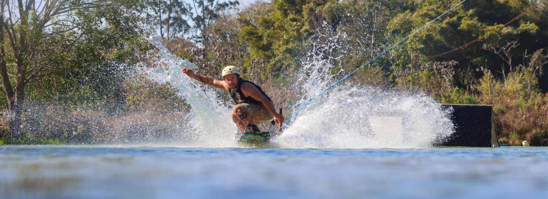 Pessoa praticando wakeboard em um lago azul, levantando um grande jato de água.
